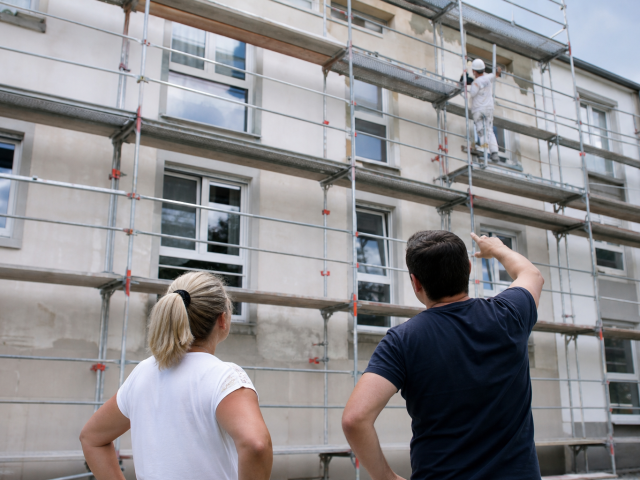 Deux personnes regardant façade d'immeuble avec échafaudage et ouvrier